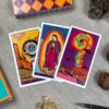 Three tarot cards—The Magician, Temperance, and Wheel of Fortune—featuring vibrant colors and cosmic themes are laid on a surface. They are surrounded by crystals, a pen, with the colorful Desert Illuminations Tarot - 1st Edition deck box in the background.