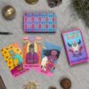 The Desert Illuminations Tarot - 2nd Edition features vibrant cards spread out on a cloth, showcasing The Trickster, The Hierophant, and Death. A box and crystals complete this mystical scene.