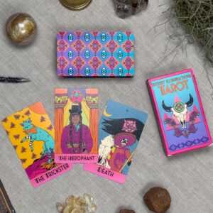 The Desert Illuminations Tarot - 2nd Edition features vibrant cards spread out on a cloth, showcasing The Trickster, The Hierophant, and Death. A box and crystals complete this mystical scene.