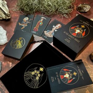 The Guidance of the Goddess Oracle set is elegantly packaged with illustrated goddess cards in a box and a black pouch featuring a gold emblem, artfully arranged with stones and dry twigs for enhanced mystical allure.