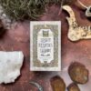 The "Spirit Keepers Tarot Revelation Edition" deck sits on a textured surface, encircled by crystals, bones, and rocks, highlighting its mystical aura in an earthy setting.