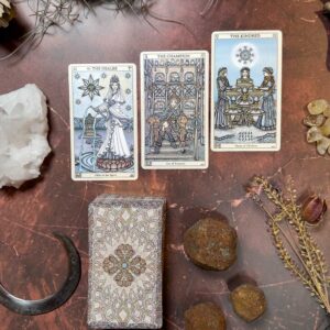 The Spirit Keepers Tarot Revelation Edition setup includes "The Healer," "The Champion," and "The Kindred" cards. Elegantly laid on a marbled surface, the display is surrounded by crystals, rocks, a decorative box, and a crescent-shaped object.