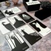 A Black Violet Tarot - Deluxe spread adorns the table with "The Fool," "The Magician," "The High Priestess," "The Empress," and "The Hierophant." The elegant black-and-white cards feature intricate illustrations, accompanied by a tarot box and decorative items.