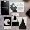 A luxurious tarot set, The Black Violet Tarot - Deluxe, sits on a marbled surface, displaying a box and monochrome cards titled "Ballerina," "The Portrait," and "Veil." This edition includes a certificate of authenticity to celebrate its unique artistry.