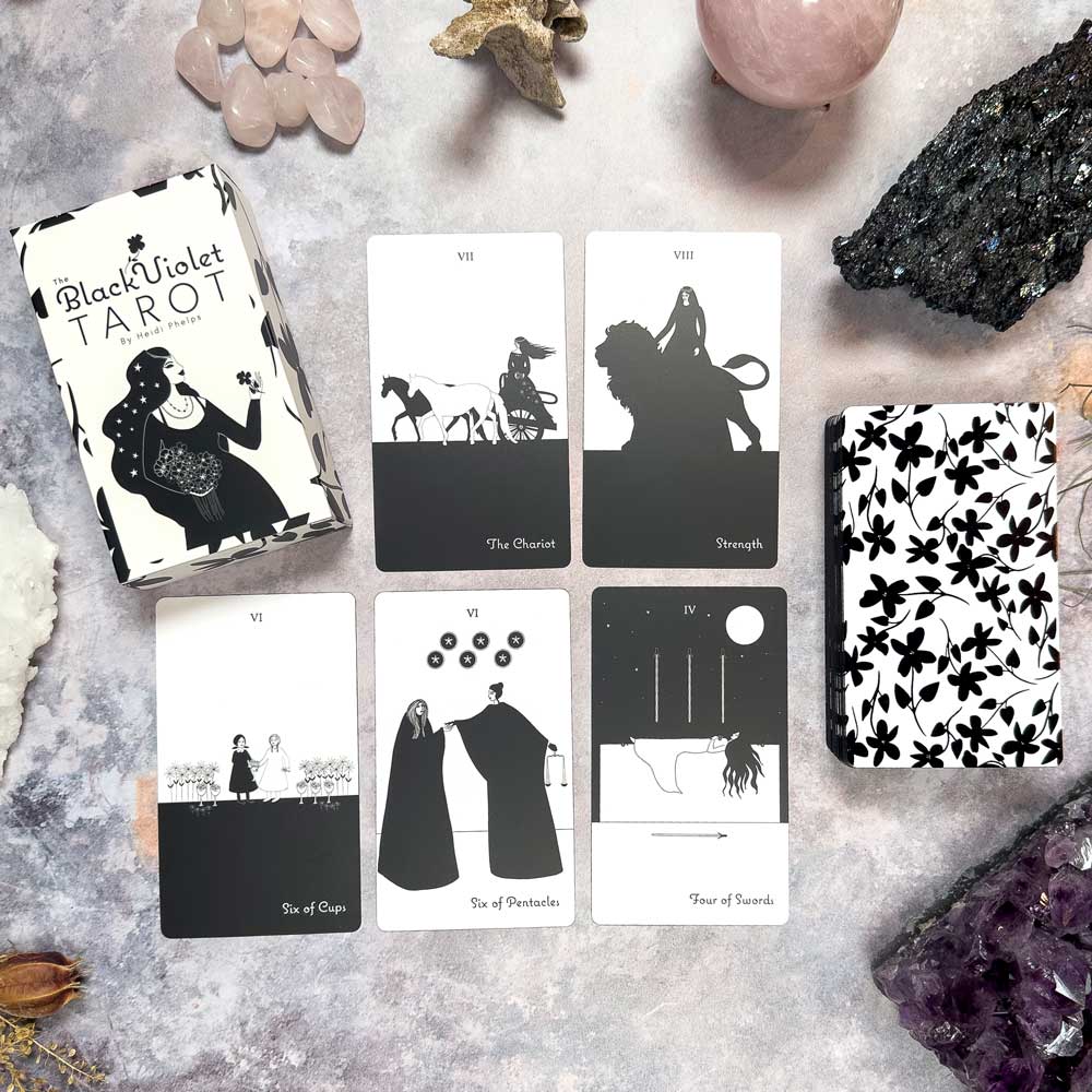 A six-card layout from The Black Violet Tarot - The White Deck, showcasing The Chariot, Strength, Six of Cups, Six of Pentacles, Four of Swords, and an abstract floral card surrounded by crystals.