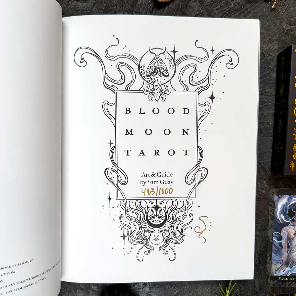 An open book shows a "Blood Moon Tarot - Deluxe" page with detailed line art, swirls, and a crescent moon. It credits "Art & Guide by Sam Guay" and features the handwritten gold edition number: 483/1000.
