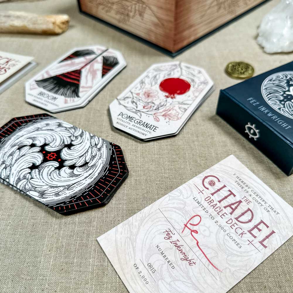 Oracle cards showcasing floral and abstract designs are spread out, with "The Citadel Oracle - LE Boxed Set" card nearby. The mystical scene is enhanced by enchanting elements like a box, crystals, and a coin.