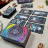 The Cosmic Visions Tarot deck, featuring vibrant cosmic artwork, is gracefully arranged on a beige cloth. The closed box with matching patterns is surrounded by an enchanting collection of crystals and stones in the foreground.