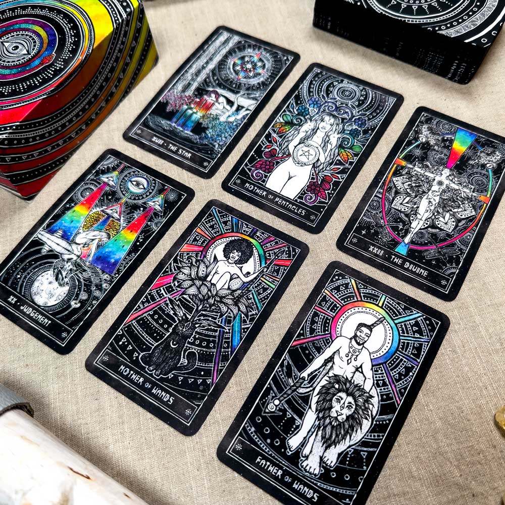 A set of six Cosmic Visions Tarot cards with intricate designs and vivid colors on dark backgrounds is laid out on a beige surface. A box with matching artwork is partially visible in the corner.