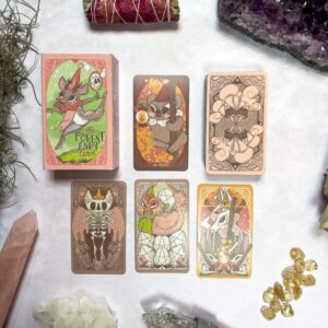 The Forest Enby Tarot set, featuring whimsical animal-themed cards, is beautifully displayed on a surface. Surrounded by crystals, dried herbs, and stones, it creates an enchanting scene that invites exploration.