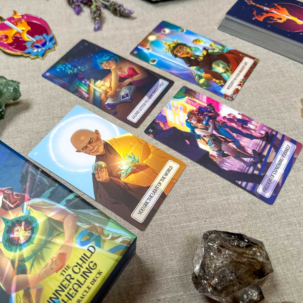 A tabletop adorned with colorful tarot cards from "The Inner Child Healing Oracle" is framed by crystals. The cards boast vibrant illustrations, including a man holding a glowing heart and a dancing couple, while a oracle box is partially visible on the side.