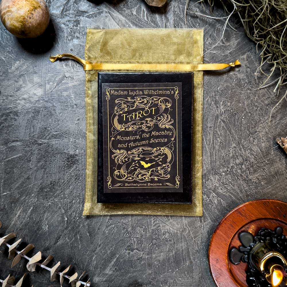 The "Madam Lydia Wilhelmina's Tarot" deck is elegantly displayed on a golden pouch surrounded by moss, a candle, and decorative items, perfectly capturing the mystical ambiance the tarot is renowned for.
