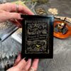 Someone holds a black box of "Madam Lydia Wilhelmina's Tarot," featuring golden designs and a bat illustration. In the background, more tarot treasures are visible alongside a small lit candle.