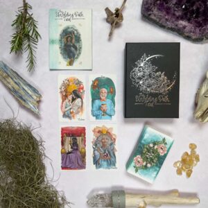 A flat lay of tarot cards, a black box with "The Unfolding Path Tarot" in silver, surrounded by crystals, moss, and a small tree branch. The cards depict diverse illustrations of people and nature, crafting an enchanting scene that suggests the journey ahead.