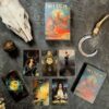 A W.I.T.C.H.-themed scene showcases the mystical W.I.T.C.H. tarot set with cards, deck box, booklet, skull, crescent blade, and textured orb on a dark surface.