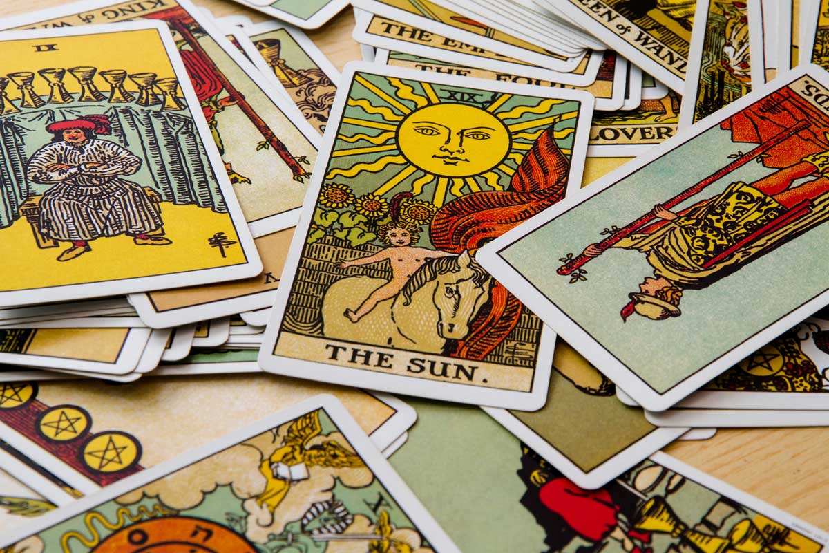 A scattered arrangement of colorful tarot cards featuring various images, including one prominently displaying "The Sun" card with a sun, child, and horse. Other visible cards show diverse symbols and illustrations.